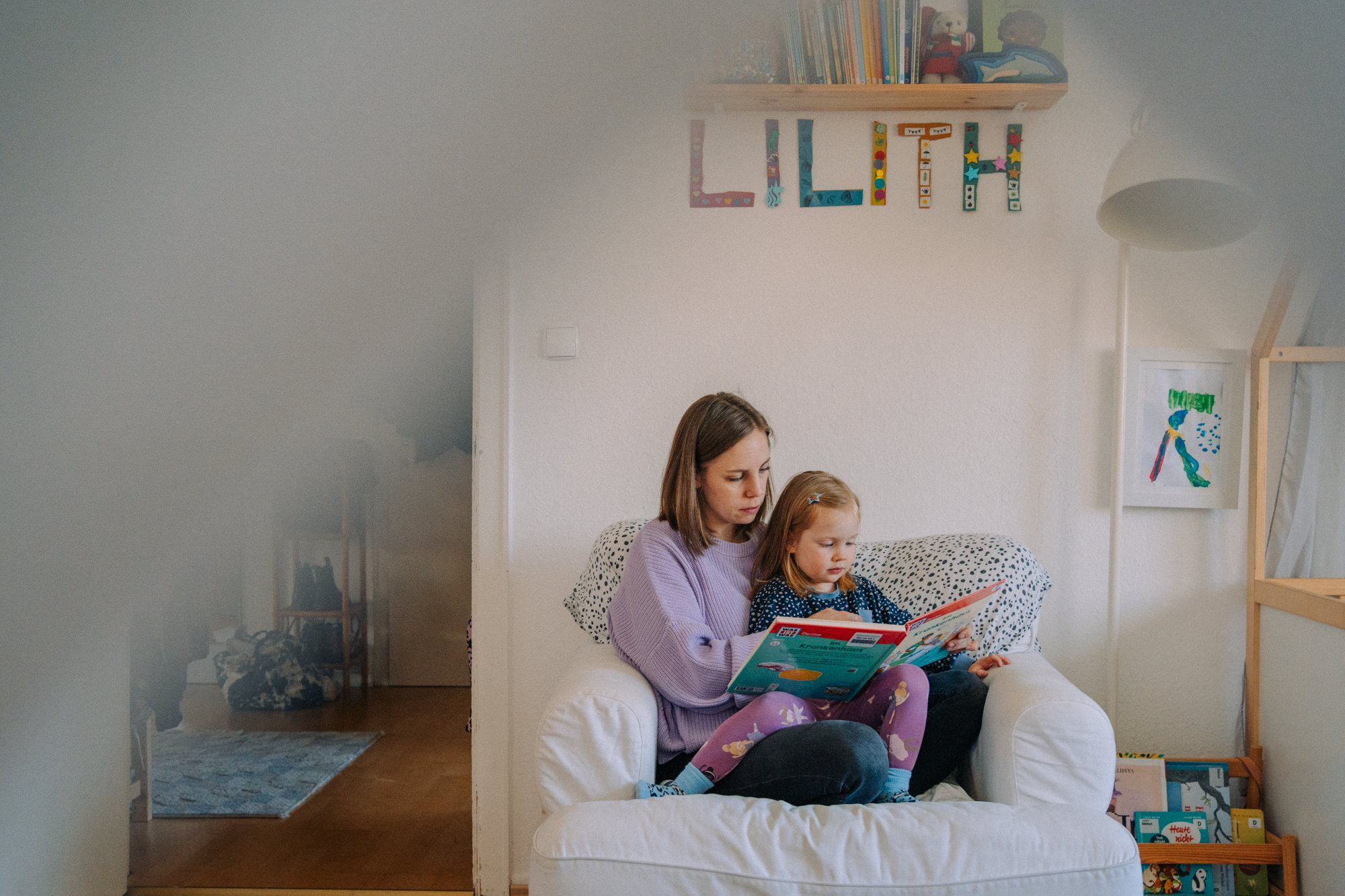 Mutter liest mit Kind auf weißem Sofa im Kinderzimmer – liebevolle Vorlesemomente in der Familienfotografie