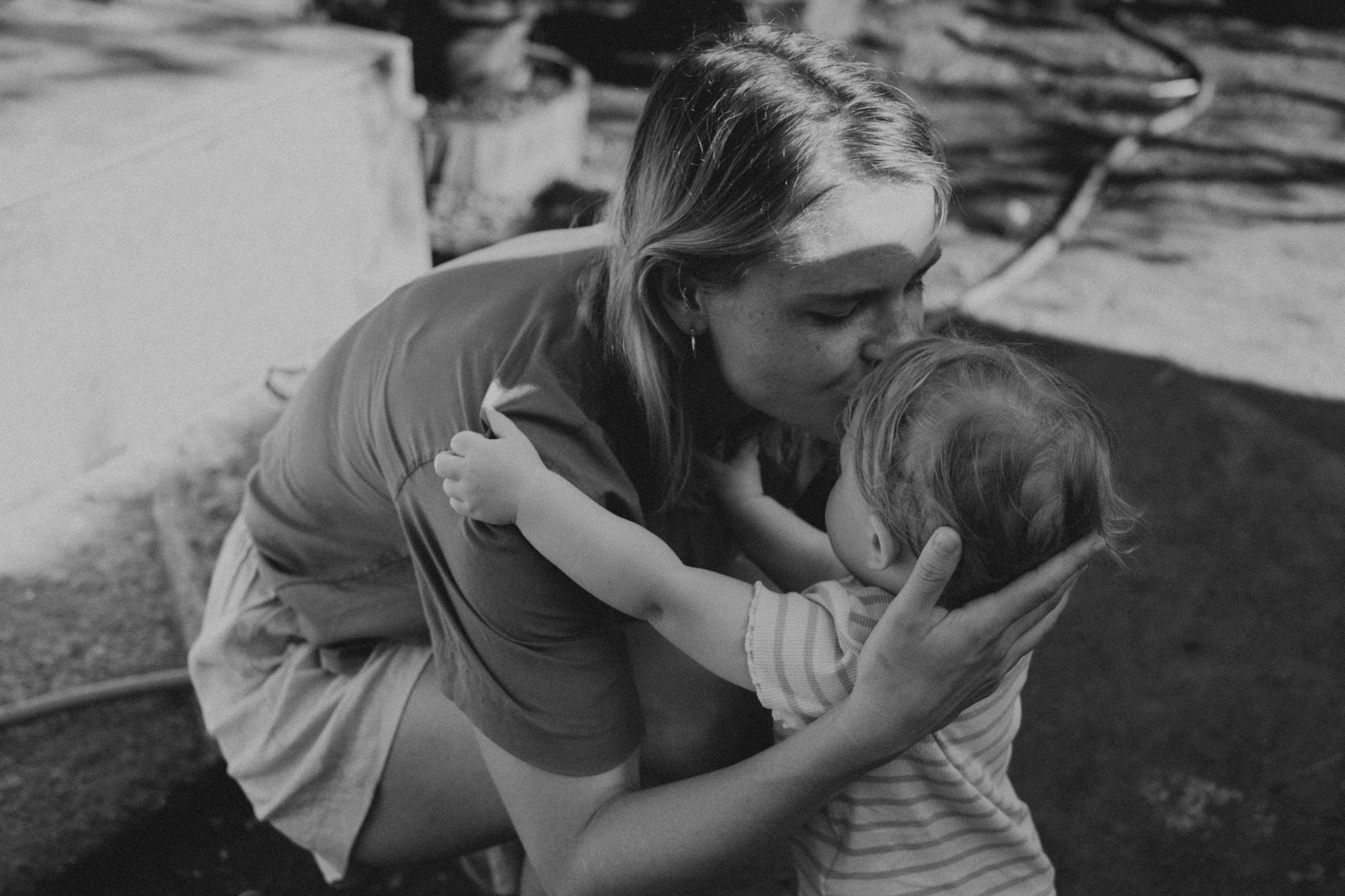 Mutter küsst Baby im Garten – emotionale Familienfotografie draußen