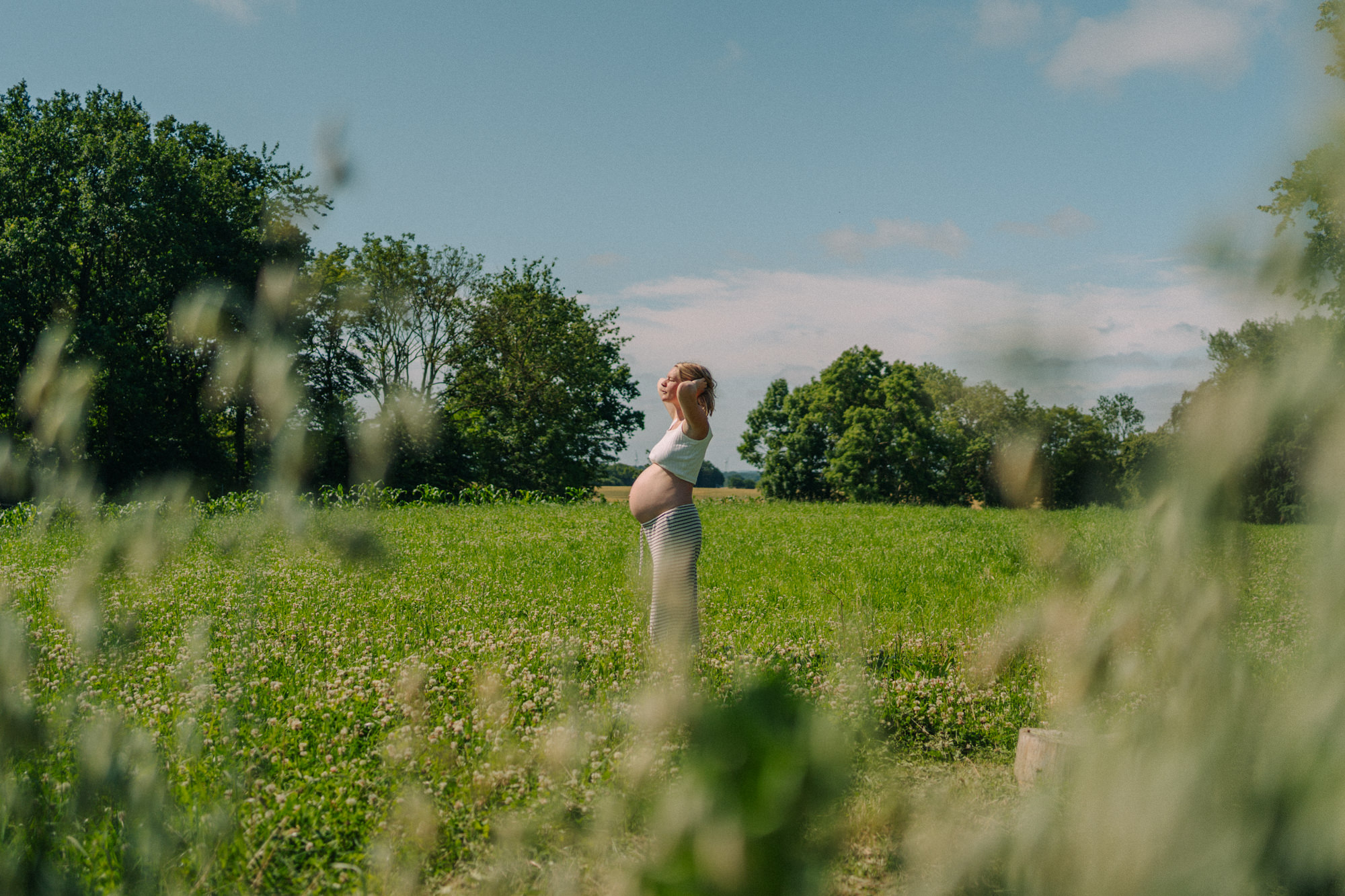 Schwangere Frau im weißen Kleid auf Wiese – Babybauchshooting Kiel im Sommer